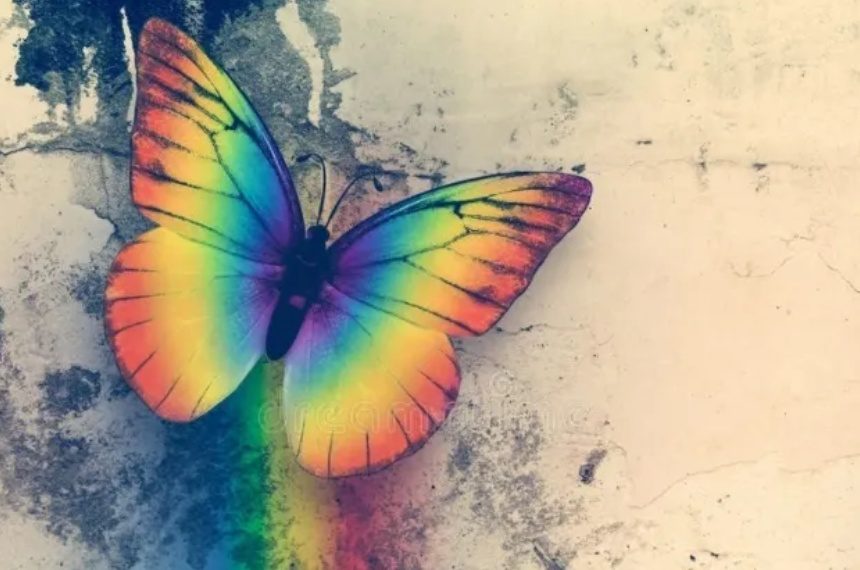 A rainbow colored butterfly sitting on top of a wall.