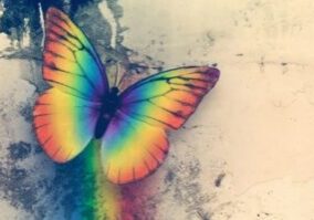 A rainbow colored butterfly sitting on top of a wall.